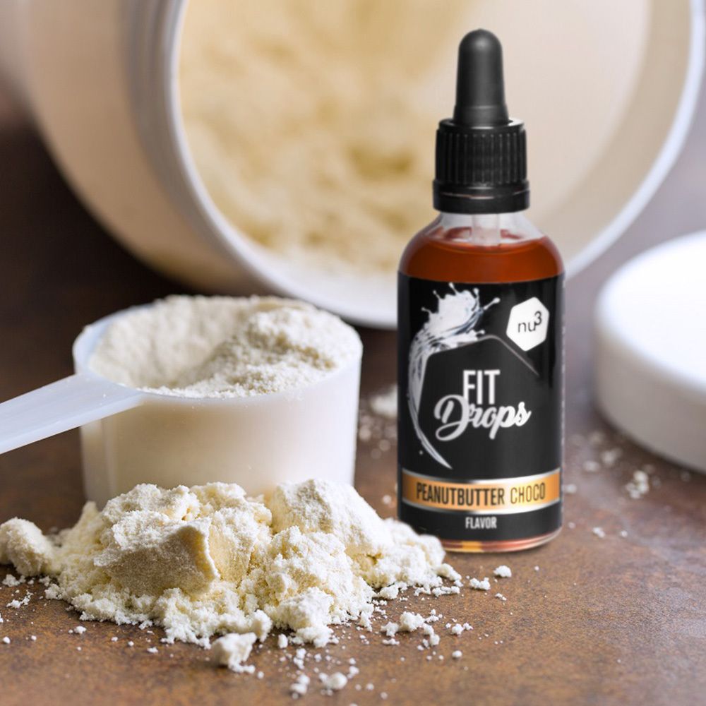 Flasche mit brauner Flüssigkeit und Tropfer neben einem Messlöffel und Proteinpulver. Aufschrift: FIT Drops Peanutbutter Choco Flavor.
