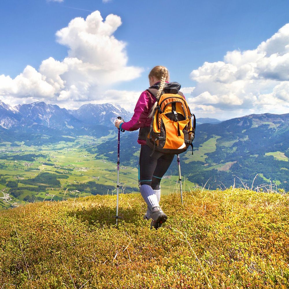 Person mit Rucksack auf einem Berg. Blick auf Berge und Tal. Wanderstöcke.