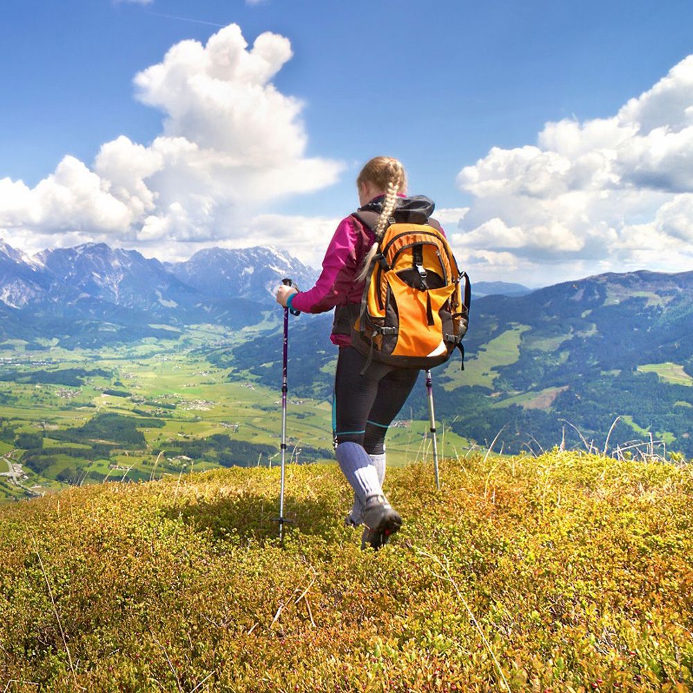 Person mit Rucksack wandert in den Bergen. Blick auf Berge und blauen Himmel mit Wolken.