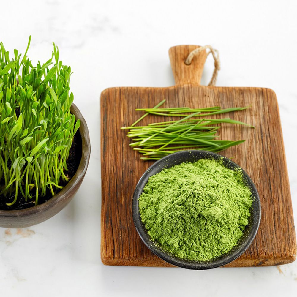 Grünes Weizengras, Pulver und frische Halme auf Holzbrett. In Schalen und auf Brett. Hintergrund: weißer Marmor.