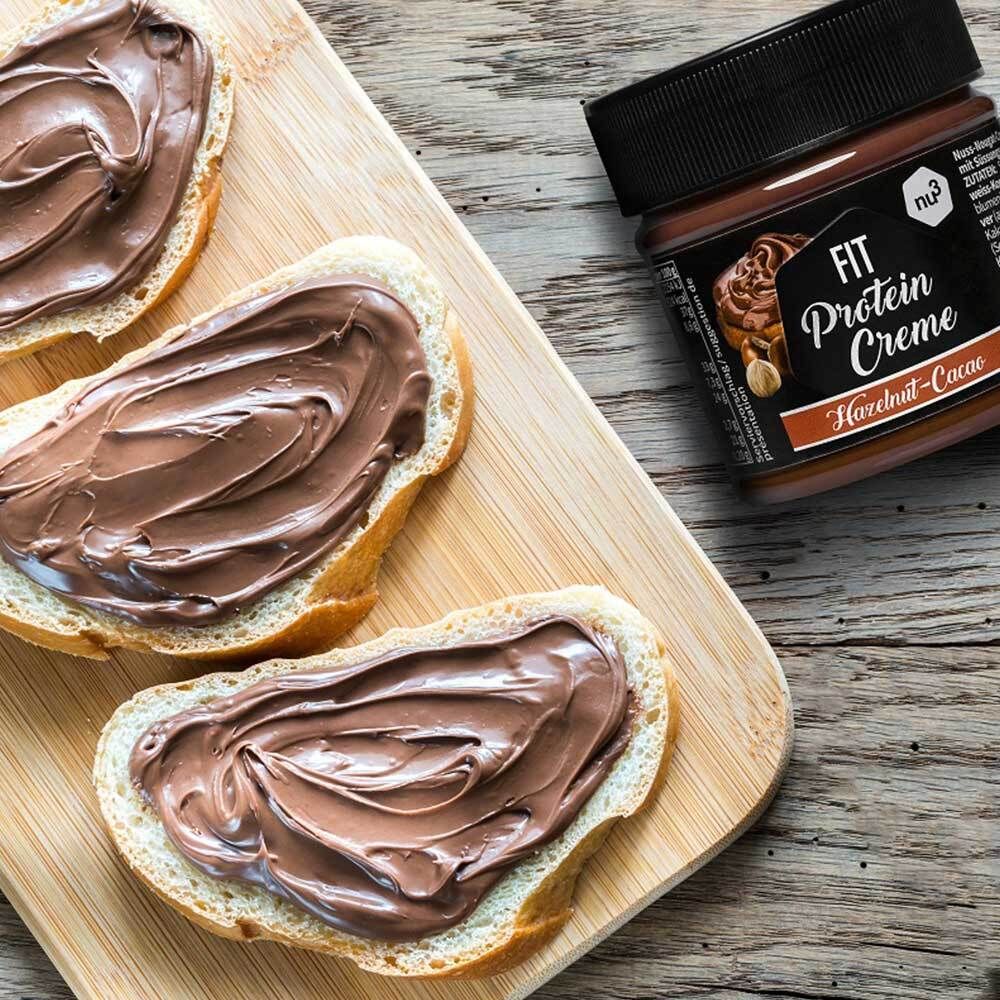 Holzbrett mit Brotscheiben, bestrichen mit Fit Protein Creme. Glas mit Creme im Hintergrund.