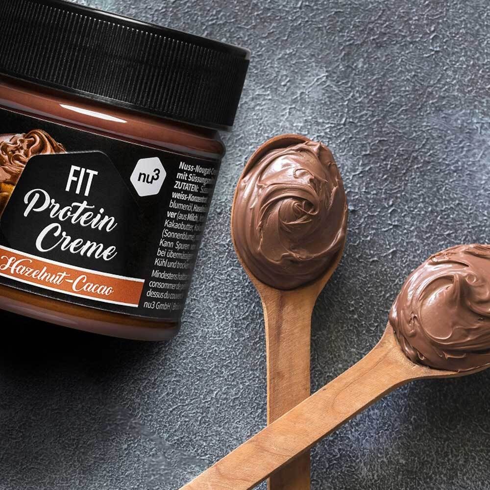 Zwei Holzlöffel mit Fit Protein Creme. Glas mit Creme im Hintergrund.