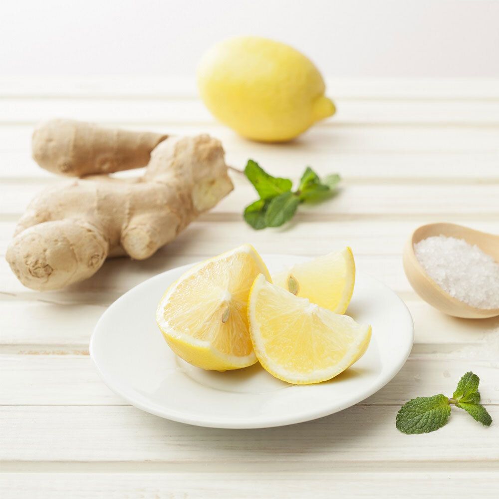 Zitronenscheiben auf einem Teller, daneben Ingwer, Minze und Salz. Auf hellem Holzuntergrund.