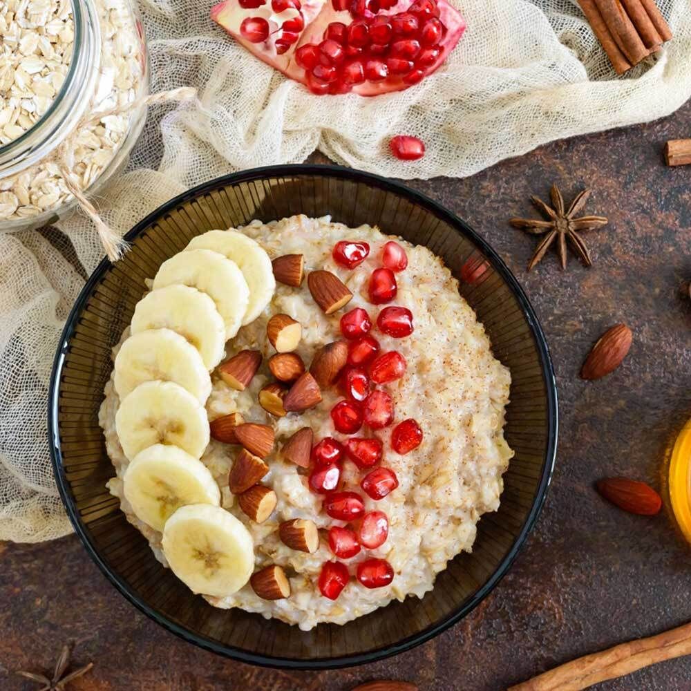 Porridge mit Bananenscheiben, Mandeln und Granatapfelkernen in Schüssel.
