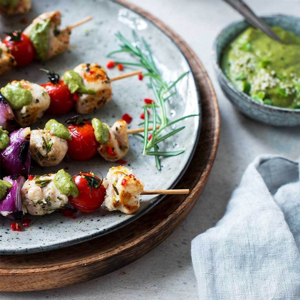 Teller mit Spießen aus Tomaten, Hähnchen und Zwiebeln. Dazu grüne Sauce und Rosmarinzweig.