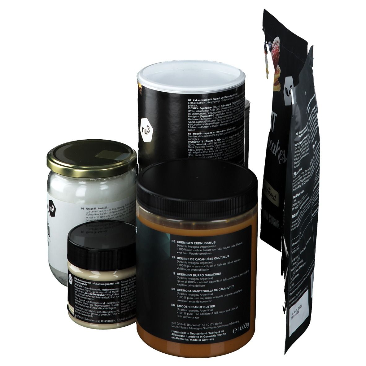 Verschiedene nu3 Produkte: Kokosöl, Erdnussbutter, Protein Creme und Pancakes. Verpackungen in Schwarz und Weiß. Rückseite mit Text.