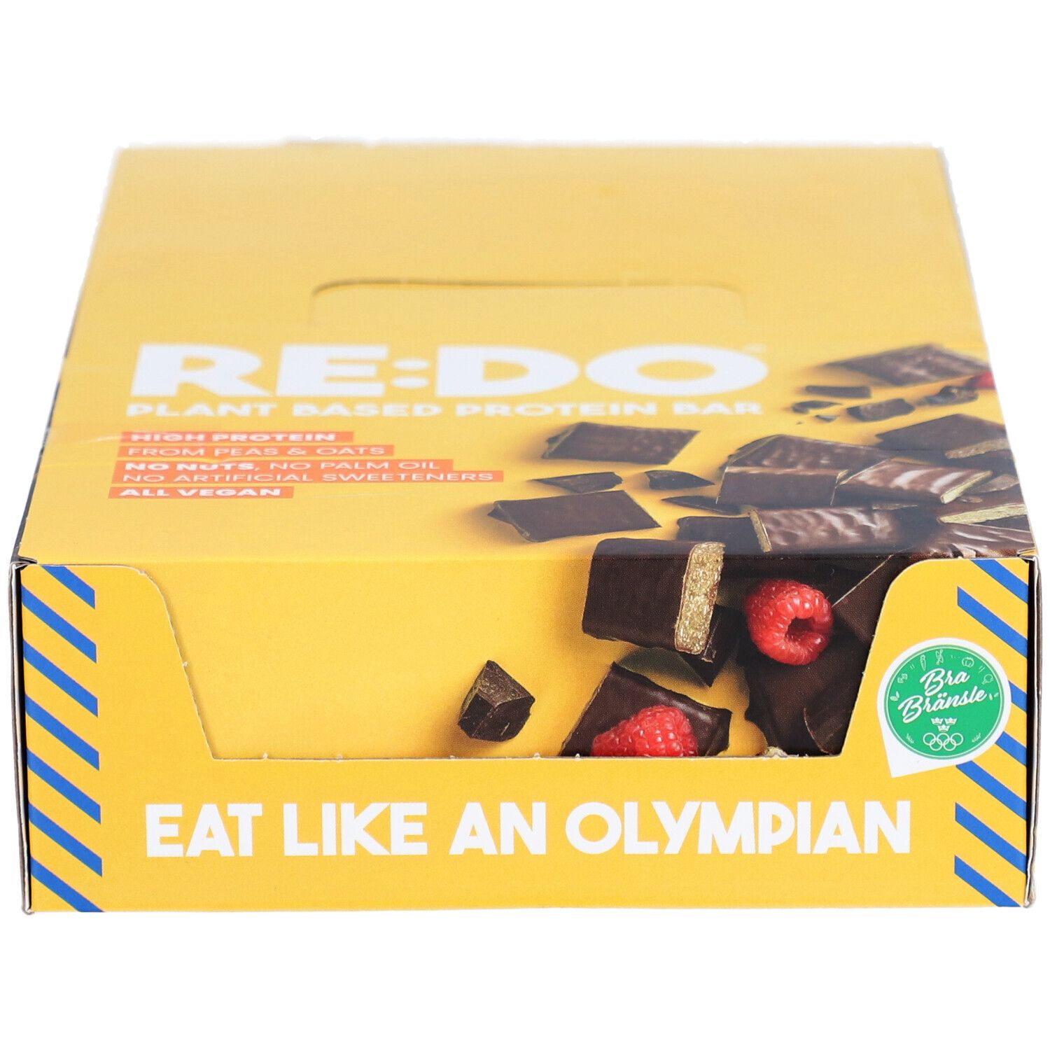 Gelbe Schachtel mit RE:DO-Schokoriegeln. Aufschrift: Plant Based Protein Bar. Sichtbar: Riegelstücke mit Himbeeren. Aufschrift: Eat like an Olympian. Vegan.