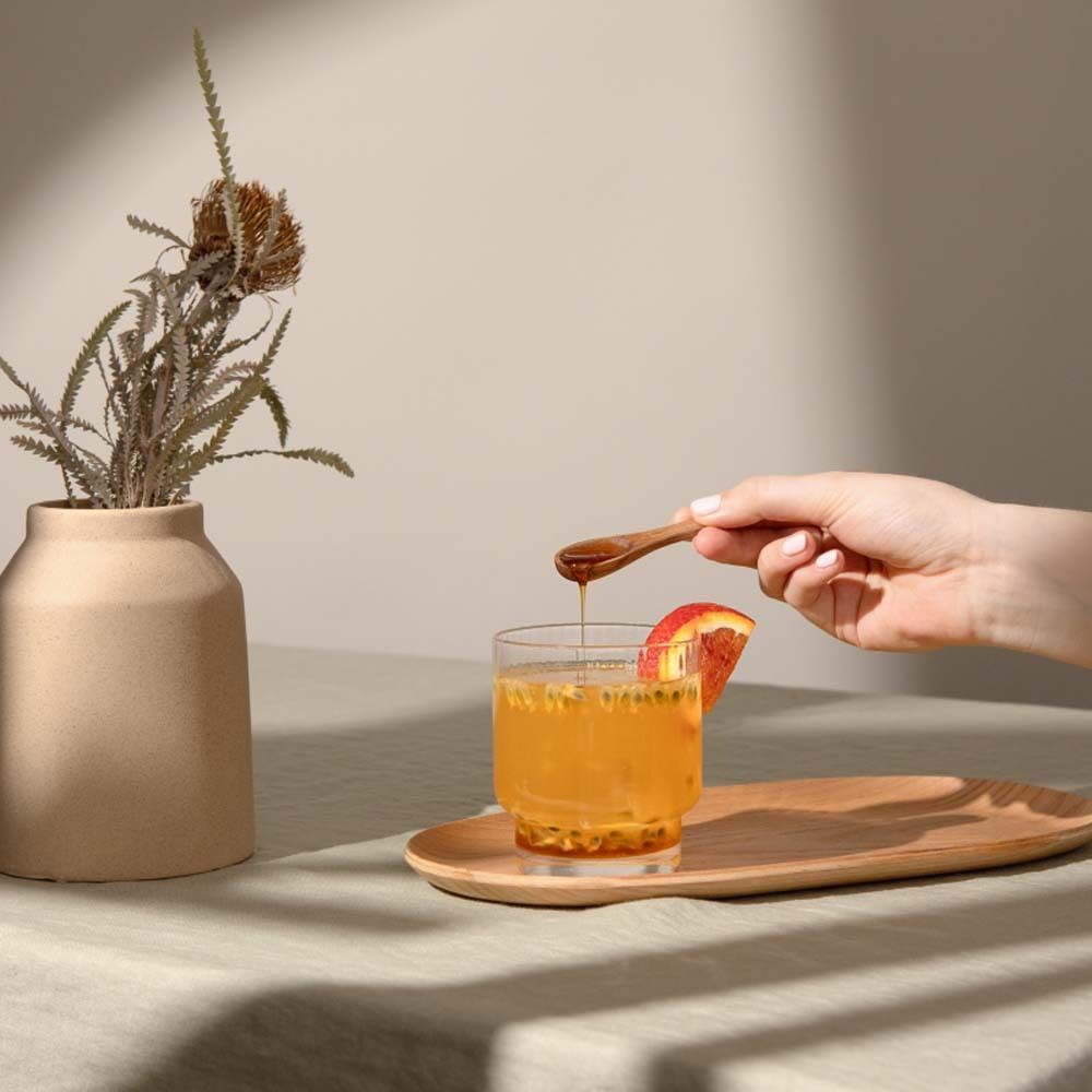 Glas mit Getränk, Holztablett, Hand mit Löffel, Vase mit Zweig.
