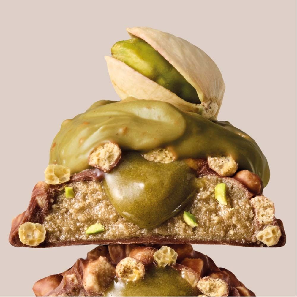 Halbierte Proteinriegel-Ansicht mit Pistazien-Topping. Sichtbare Zutaten: Pistazien, Nüsse, Schicht mit Creme.