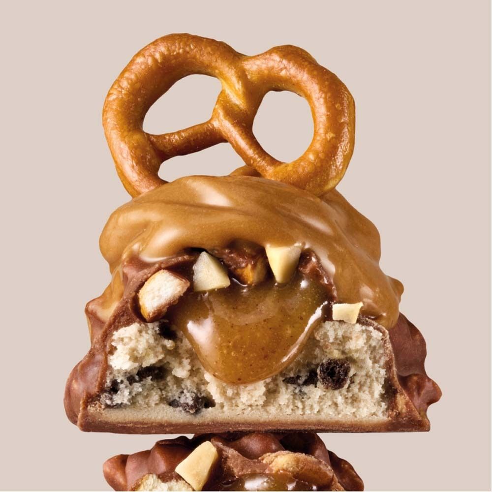 Proteinriegel-Querschnitt mit Erdnuss, Brezel und Karamell. Sichtbare Zutaten und Schokoladenüberzug.