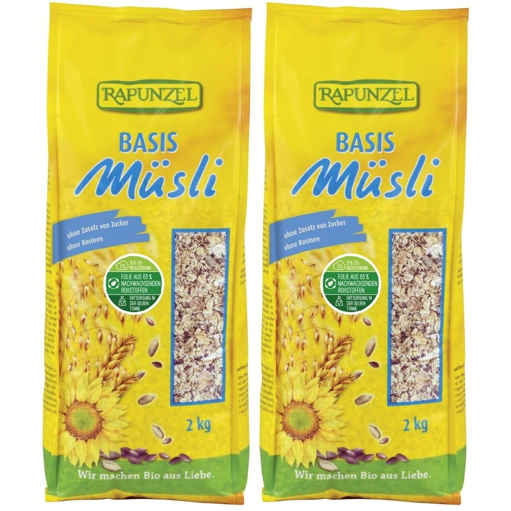 Zwei gelbe Beutel RAPUNZEL Basis Müsli. Aufdrucke: ohne Zuckerzusatz, 2 kg, Bio-Siegel. Abbildung von Sonnenblumen und Getreide.