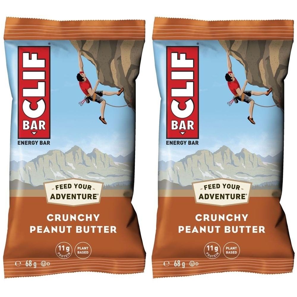 Zwei CLIF Bar Energieriegel mit Crunchy Peanut Butter. Verpackung mit Bergsteiger-Illustration. Text: "Crunchy Peanut Butter", "11g Protein", "Plant Based".