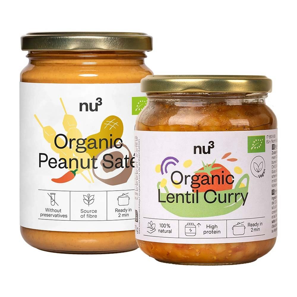 Zwei Gläser mit Aufschrift "nu3 Organic Peanut Saté" und "Organic Lentil Curry". Gläser mit goldenen Deckeln und weißen Etiketten.
