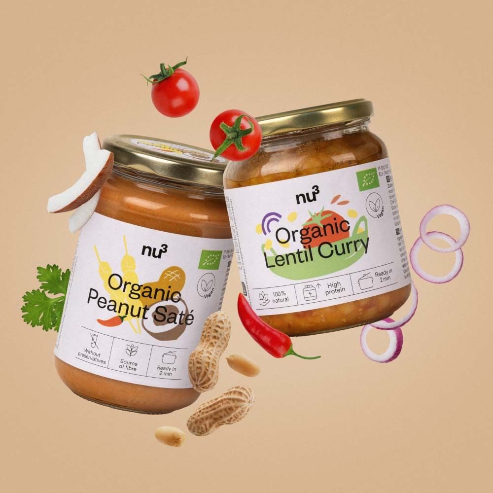 Zwei Gläser "nu3 Organic Peanut Saté" und "Organic Lentil Curry" mit Zutaten wie Tomaten, Erdnüssen und Kokosnuss.