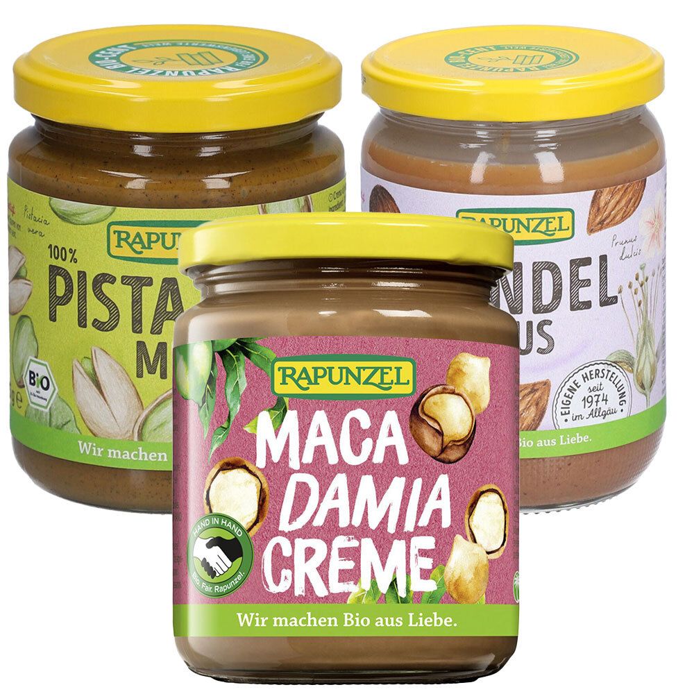 Drei Gläser Nussmus. Etiketten mit "Pistazienmus", "Mandelmus" und "Macadamia Creme". Gelbe Deckel. Marke: Rapunzel. Bio-Siegel.