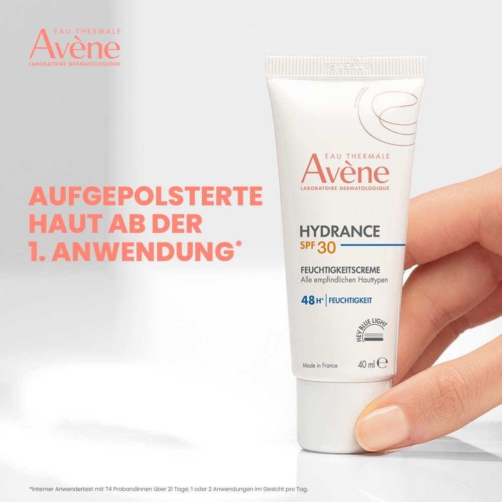 Hand hält Avène Hydrance Feuchtigkeitscreme SPF 30. Text: Aufgepolsterte Haut ab der 1. Anwendung. Tube weiß mit roter Schrift, 40 ml.