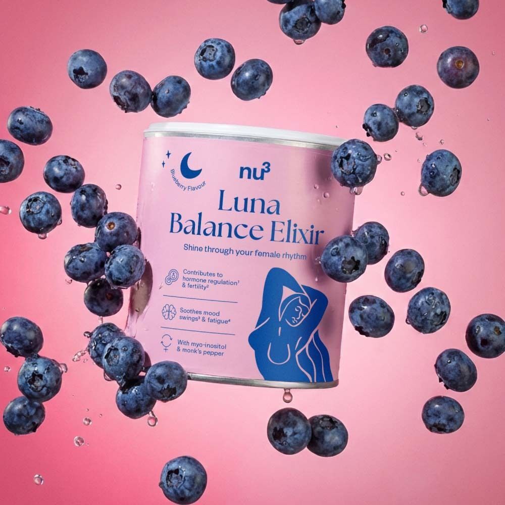 Dose nu3 Luna Balance Elixir, umgeben von Blaubeeren. Rosa Hintergrund. Auf der Dose steht Luna Balance Elixir, Blaubeer-Geschmack.