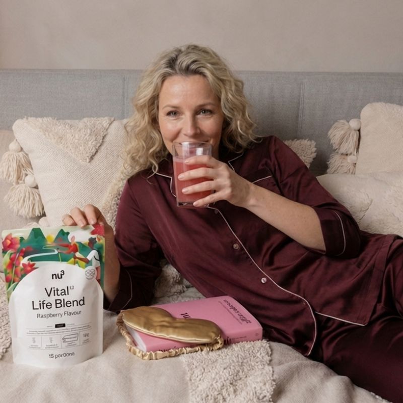 Frau trinkt nu3 Vital Life Blend Himbeergeschmack im Bett mit Verpackung.
