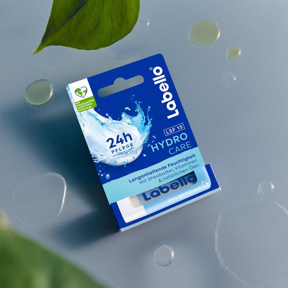 Labello Hydro Care Lippenbalsam-Verpackung auf einem grauen Hintergrund mit Wassertropfen und Blättern.