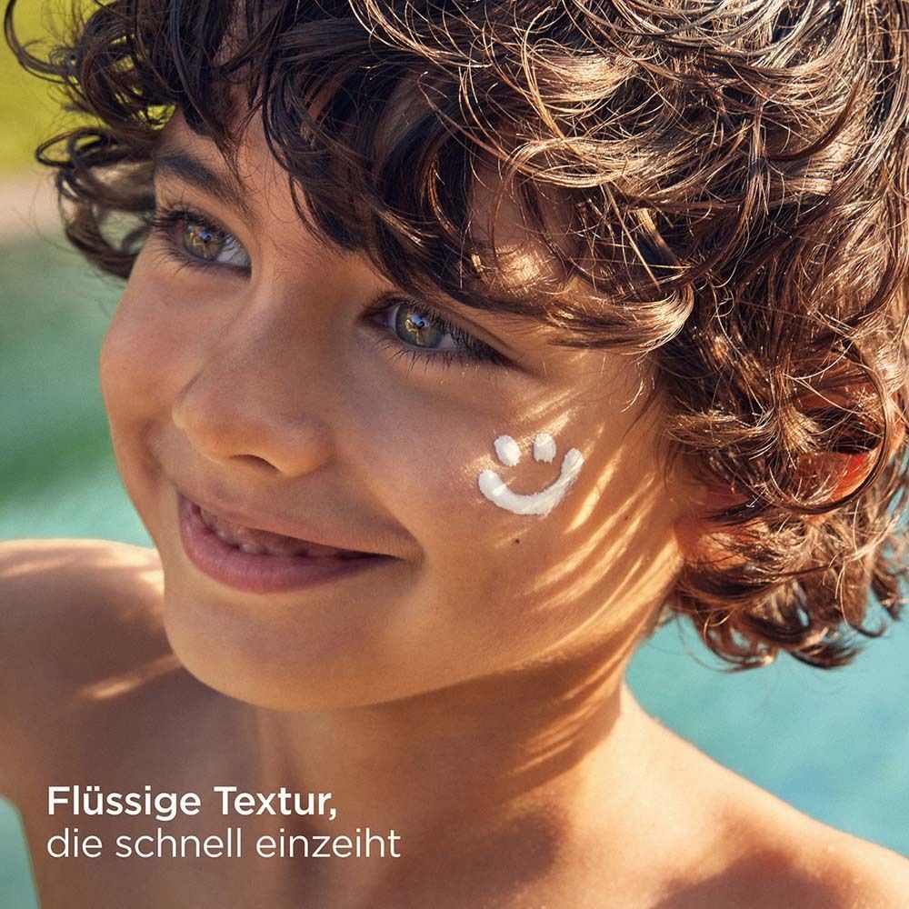 Kind mit Sonnencreme-Smiley auf der Wange. Text: Flüssige Textur, die schnell einzieht.
