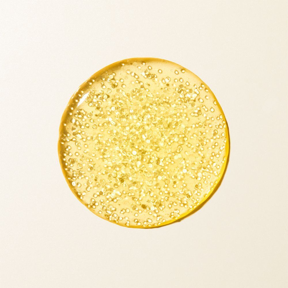 Ein goldfarbener Tropfen NUXE Super Serum [10]. Runde Form mit kleinen Partikeln. Auf hellem Hintergrund.