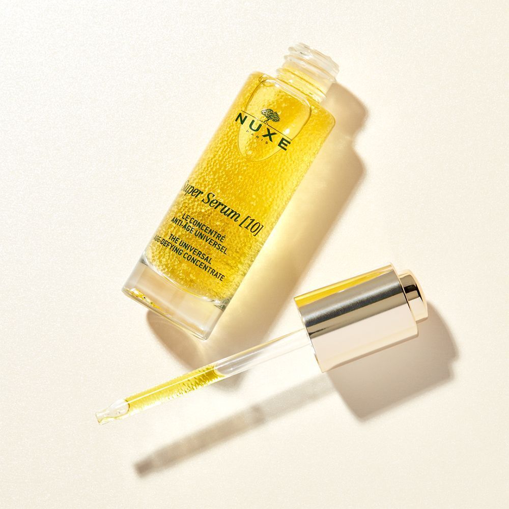 NUXE Super Serum [10] Flasche mit geöffnetem Deckel und Pipette. Goldfarbene Flüssigkeit. Pipette liegt daneben.