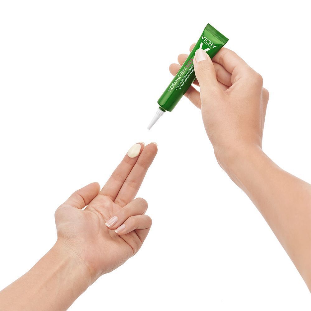 Hände halten eine grüne Tube. Creme wird auf den Finger aufgetragen. Marke VICHY.