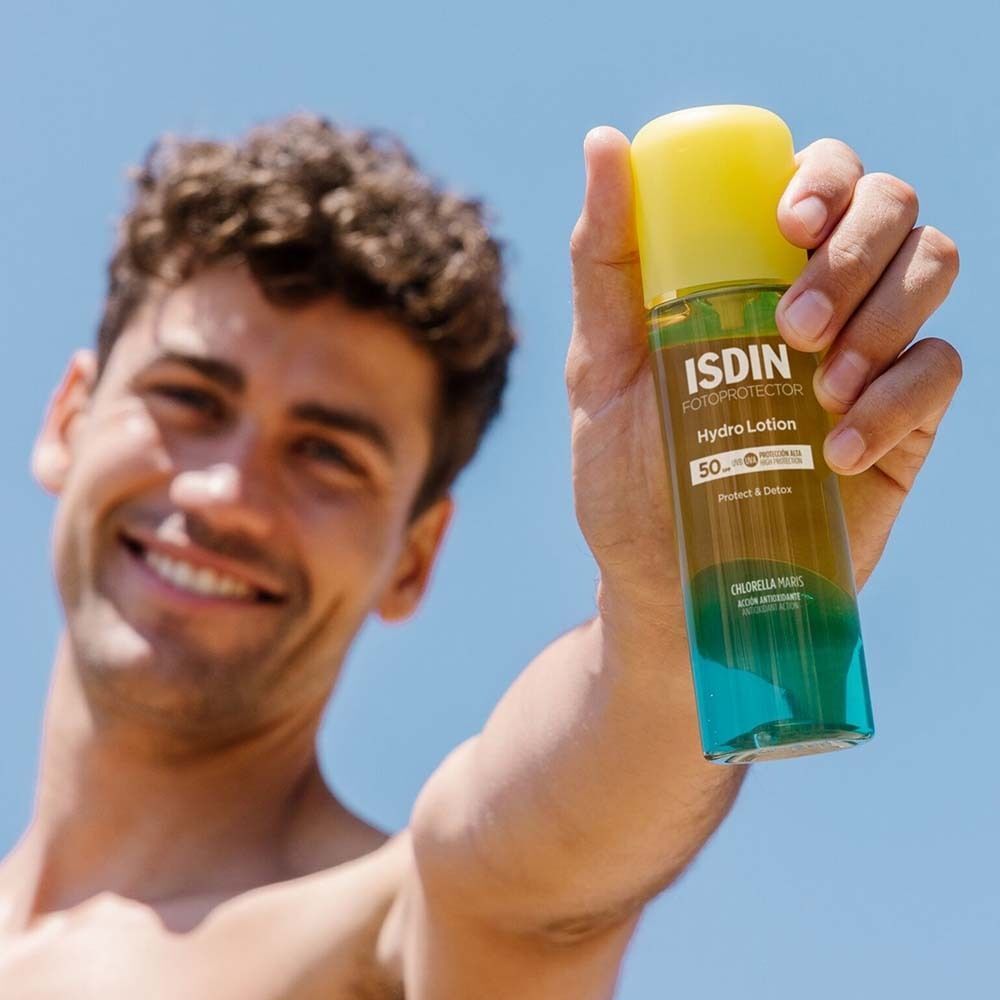Mann hält eine Flasche mit gelbem Deckel und blau-grünem Boden. Aufschrift: ISDIN Hydro Lotion 50. Chlorella Maris.