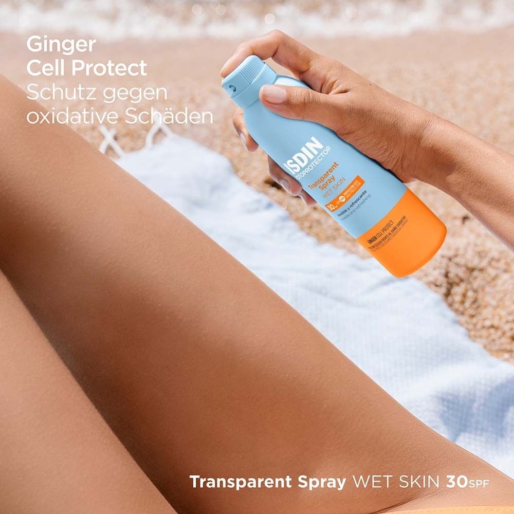Person sprüht auf ein Bein mit einer blauen Flasche. Aufschrift: ISDIN Fotoprotector Transparent Spray Wet Skin 30.