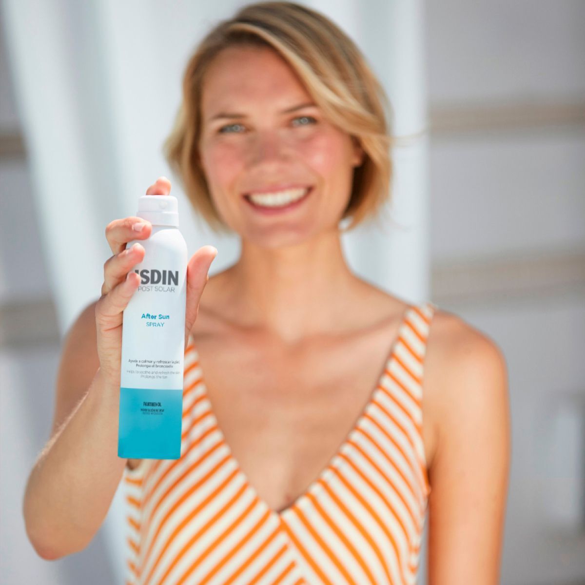 Frau hält eine weiße Sprühflasche mit blauem Boden. Aufschrift: ISDIN POST SOLAR After Sun SPRAY.