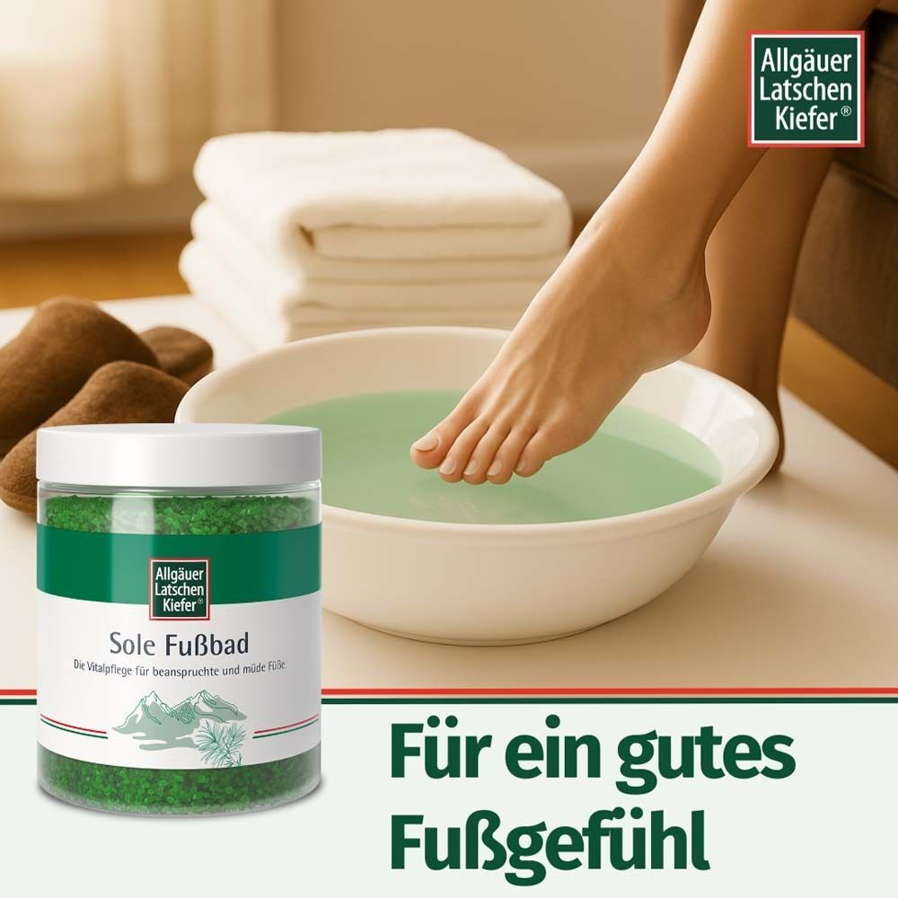 Fuß in einer weißen Schüssel mit grünem Wasser. Neben dem Fußbad-Produkt, Handtücher und Accessoires. Logo oben rechts.