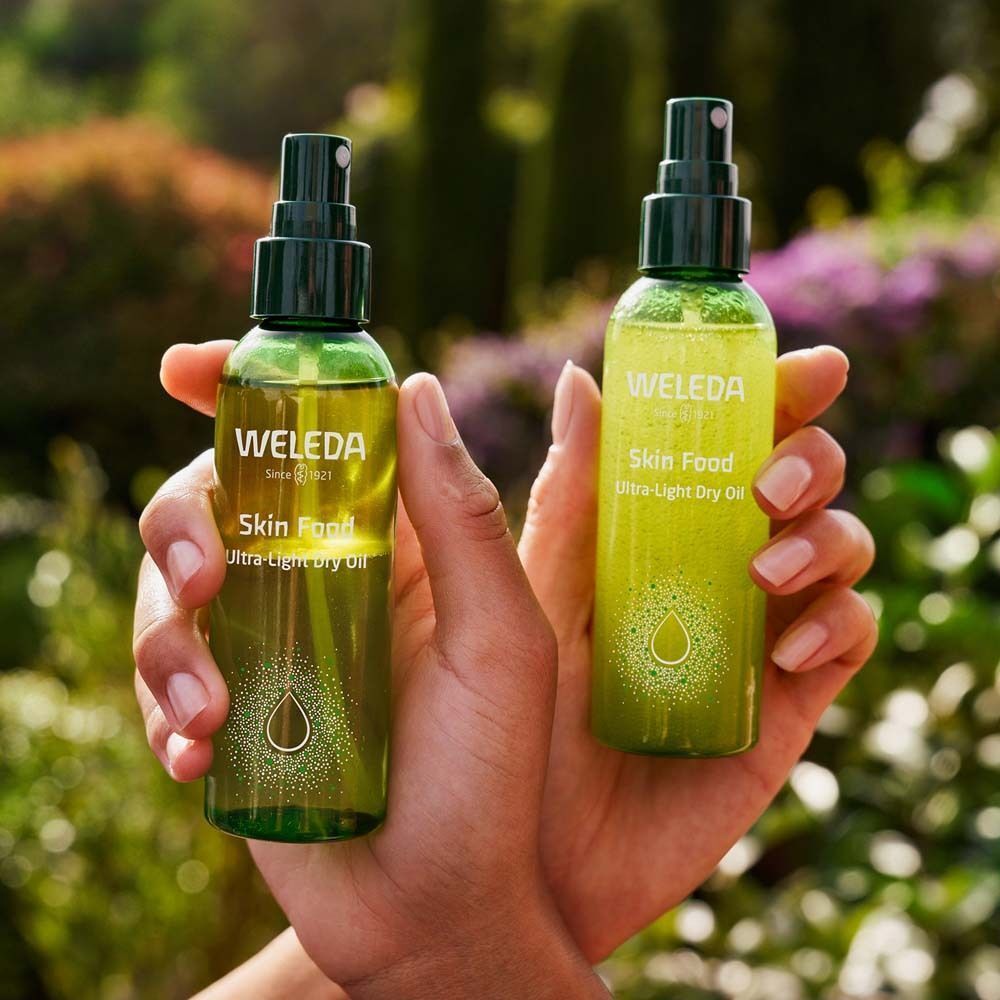 Zwei Flaschen WELEDA Skin Food Ultra-Light Dry Oil in Händen. Grüne Flaschen mit Sprühköpfen.