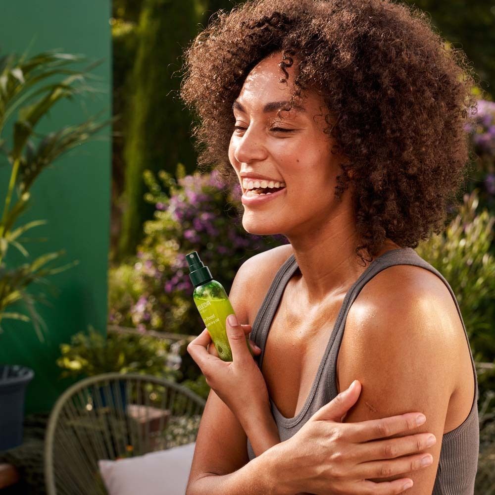Person hält eine Flasche WELEDA Skin Food Ultra-Light Dry Oil. Person trägt ein graues Tanktop.