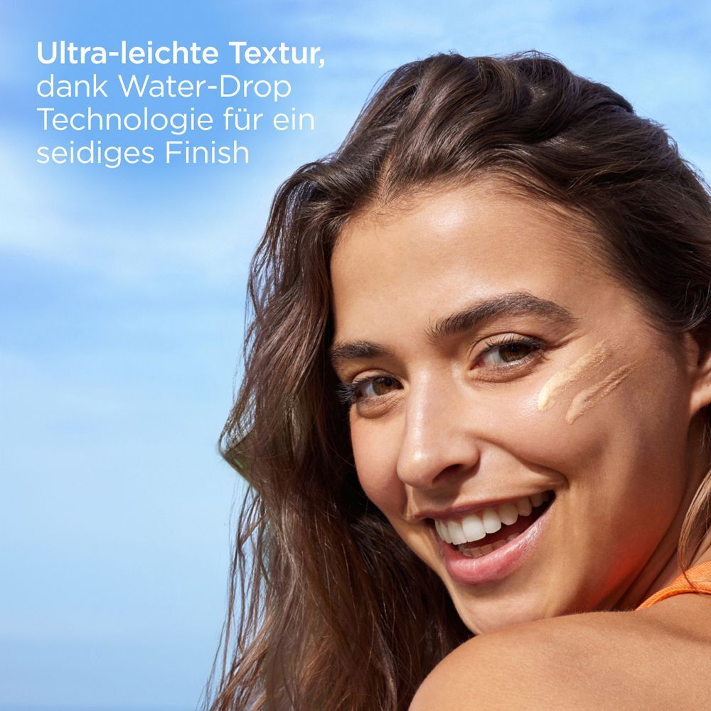 Frau mit aufgetragener Sonnencreme auf der Wange. Text: Ultra-leichte Textur, dank Water-Drop Technologie für ein seidiges Finish.
