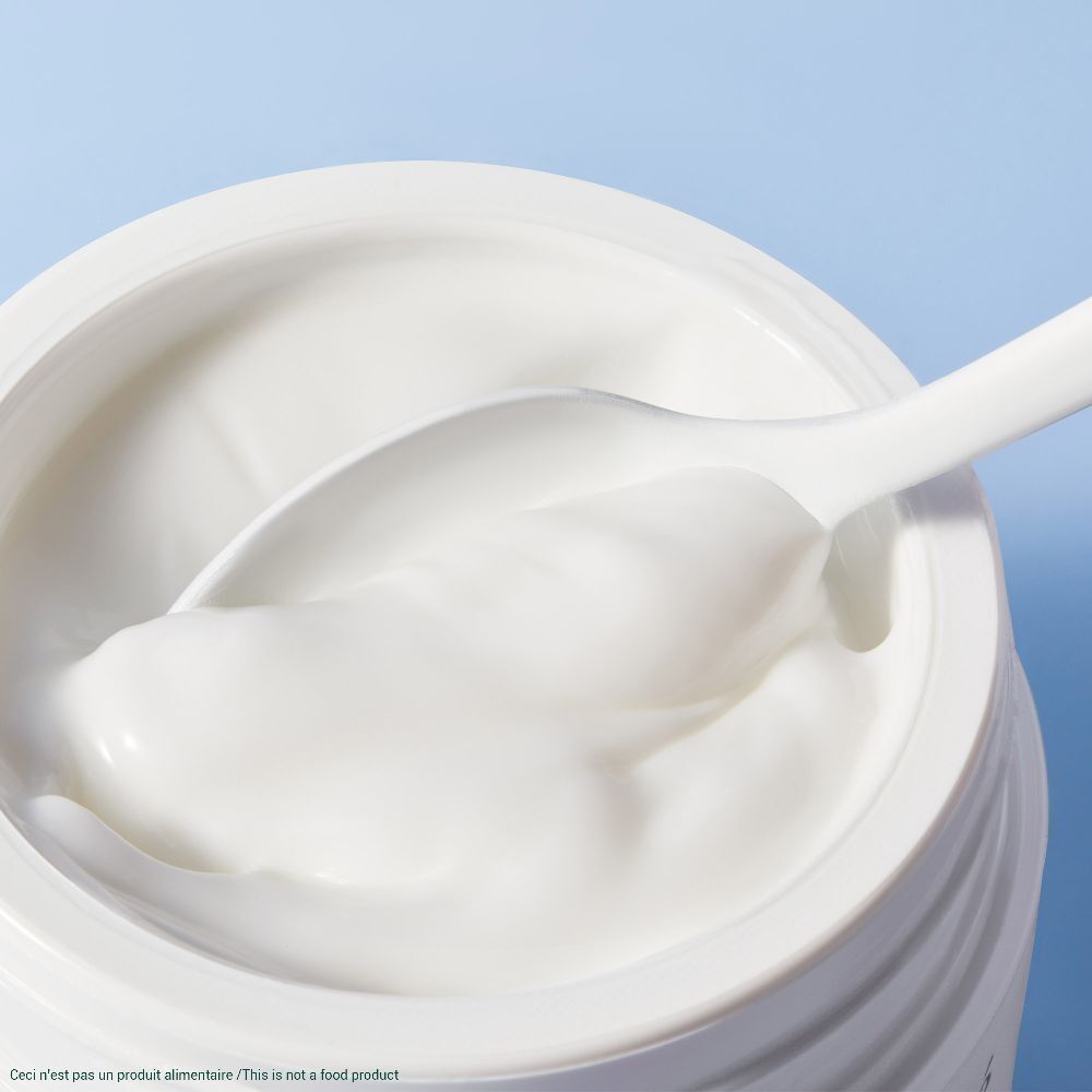 Weißes Creme Produkt in einem Tiegel. Ein weißer Löffel taucht in die Creme ein.