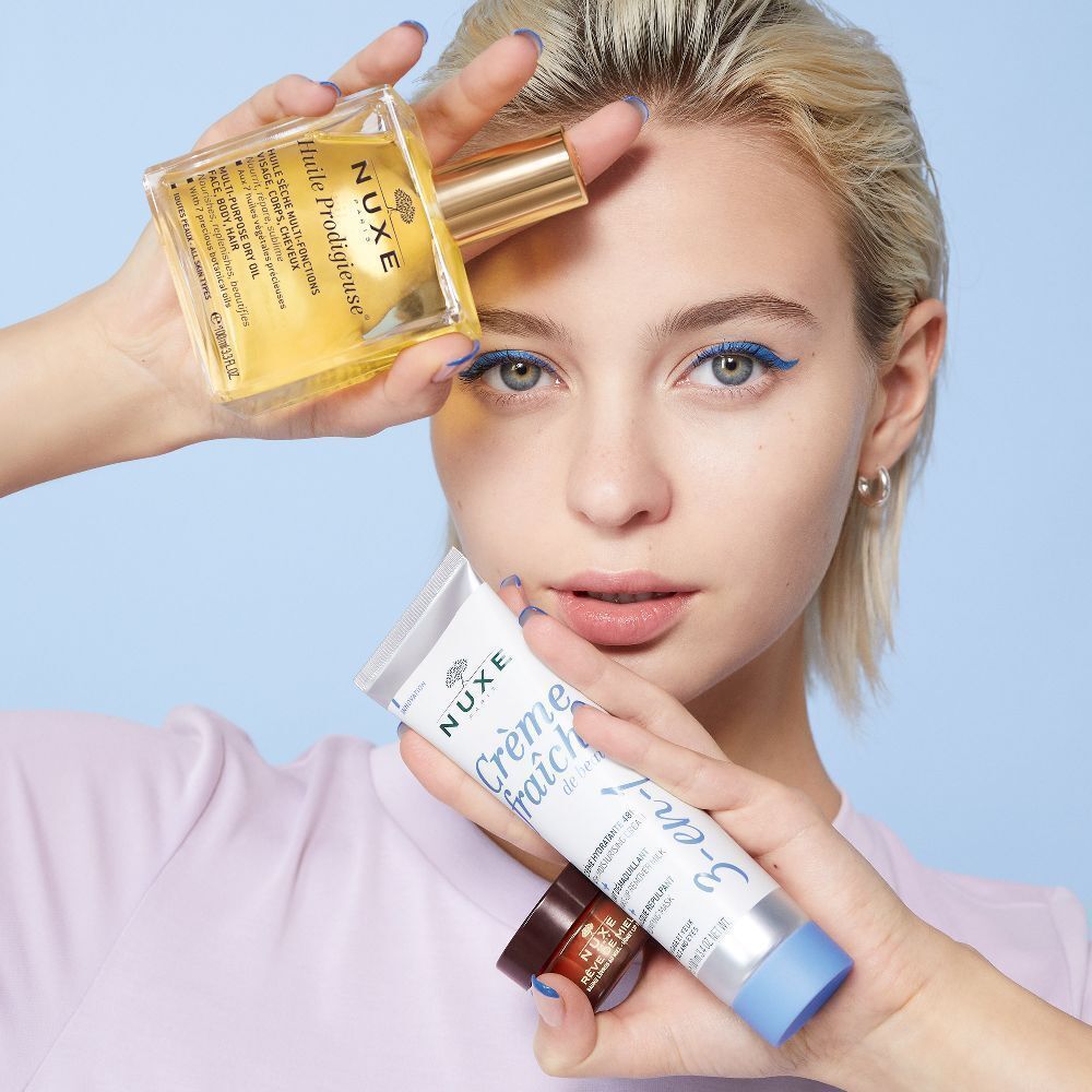 Frau hält NUXE Produkte: Öl, Tube Crème Fraîche, Lippenbalsam und ein weiteres Produkt.