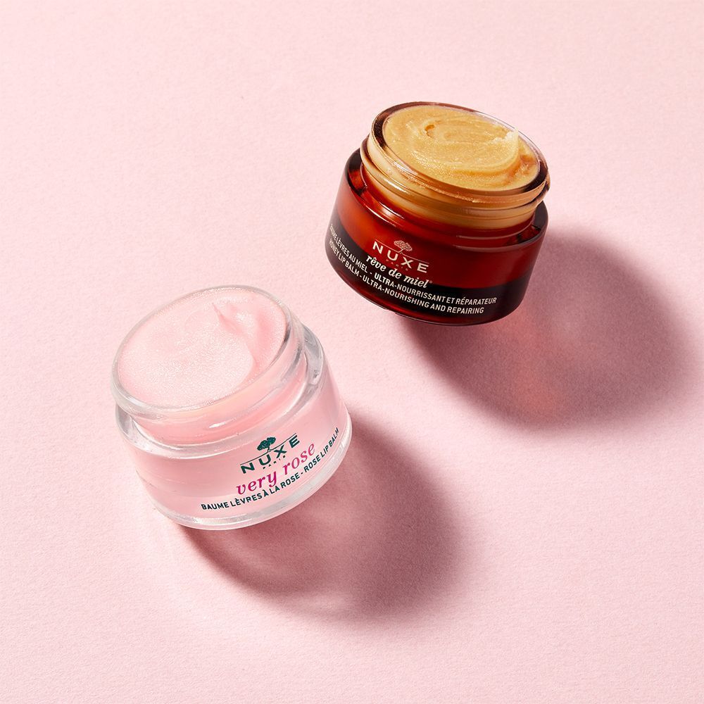 Zwei Tiegel auf rosa Untergrund. Einer mit rosa Lippenbalsam, einer mit goldfarbener Creme. Aufschrift: NUXE.