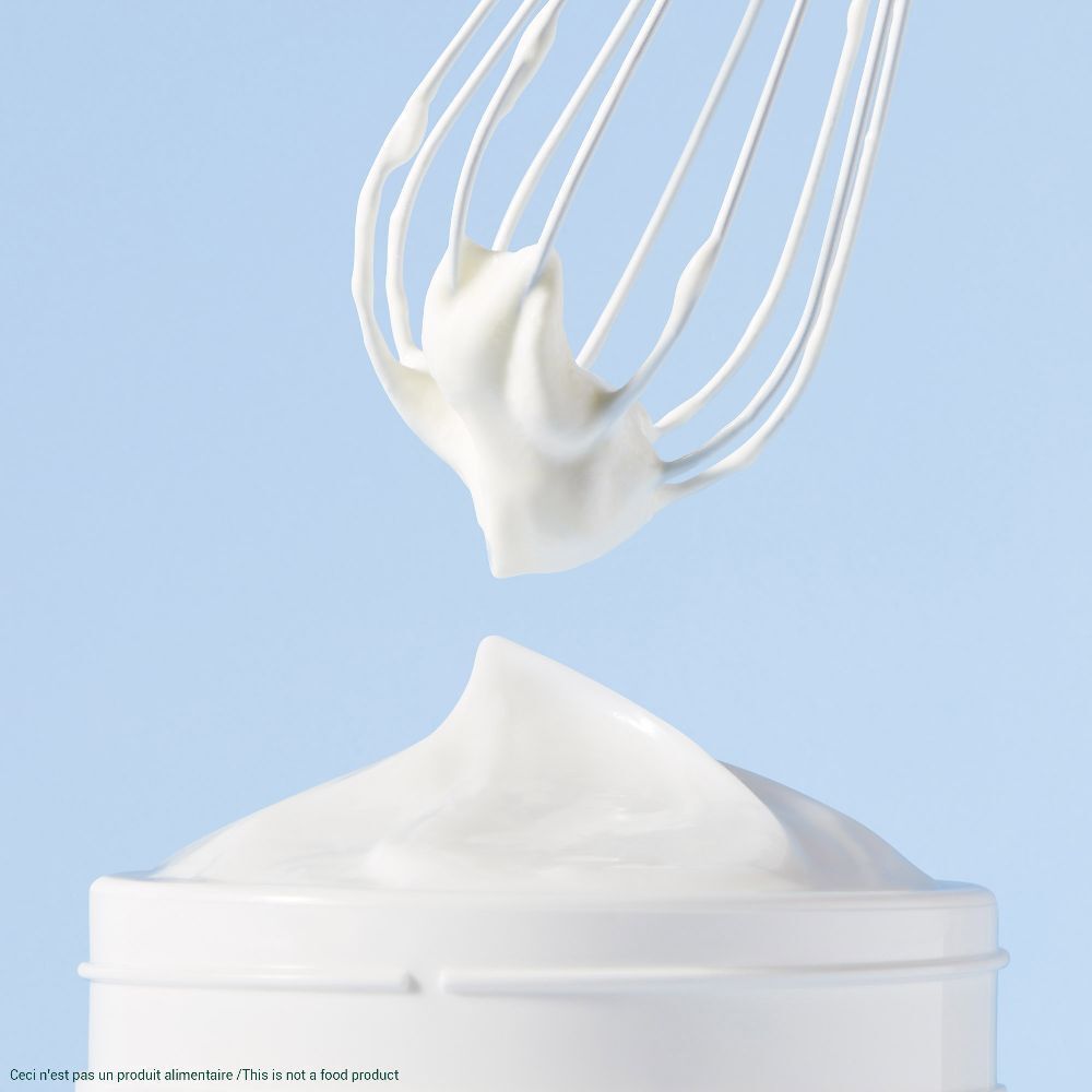 Weißer Creme-Klecks auf einem weißen Tiegel, darunter ein Schneebesen. Text: Ceci n'est pas un produit alimentaire/This is not a food product.