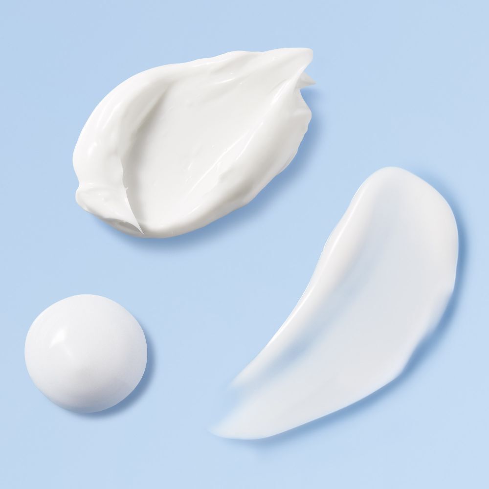 Drei Creme-Kleckse in verschiedenen Formen. Auf blauem Hintergrund. Keine Produktnamen oder Marken.