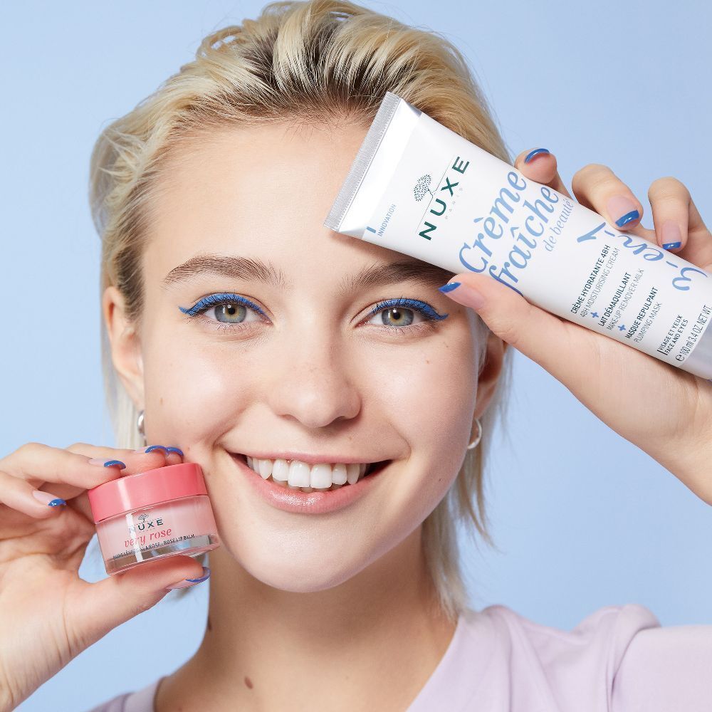 Frau hält Produkte von NUXE. Eine Tube Crème fraîche de beauté und ein Tiegel. Blaue Eyeliner.