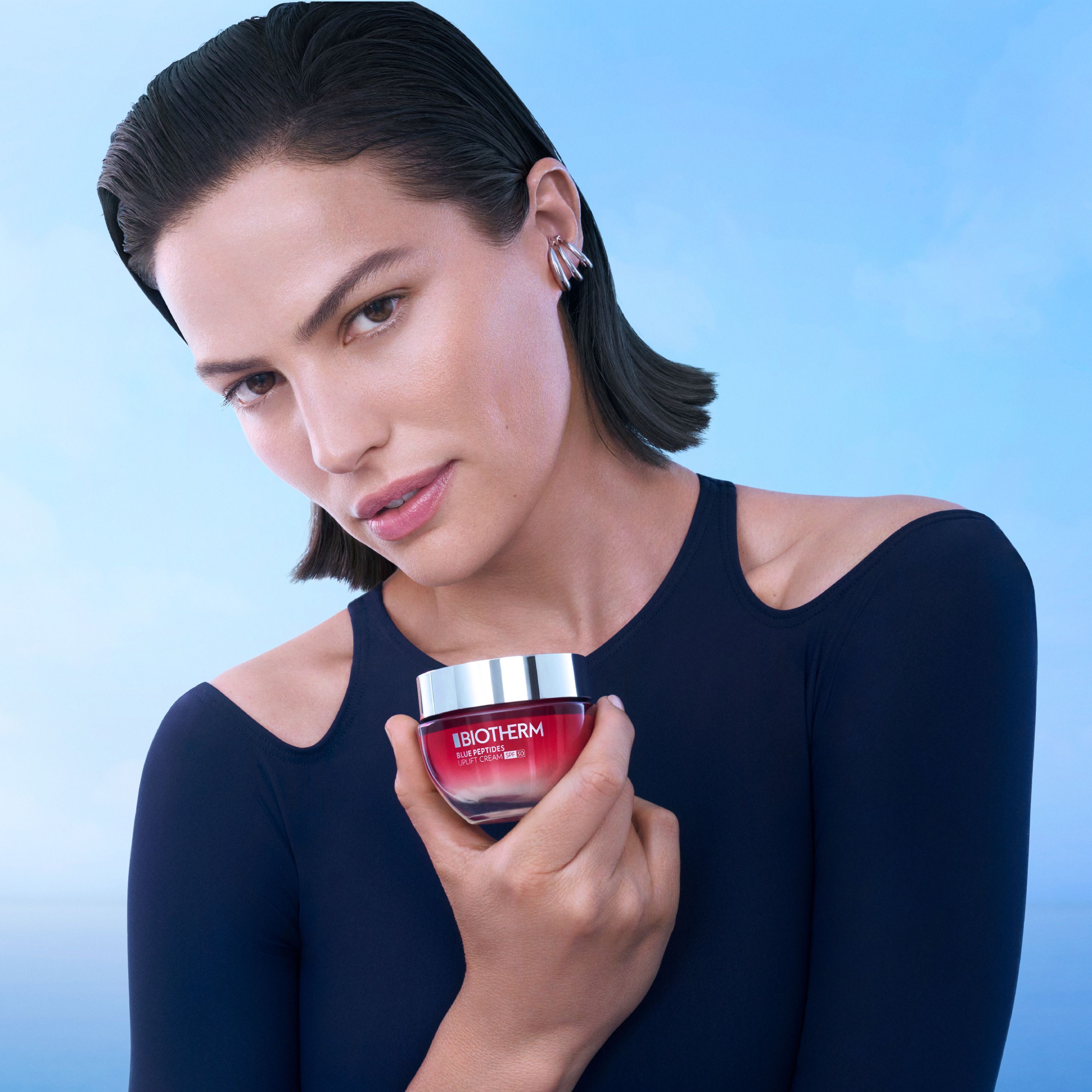Frau hält Tiegel Biotherm Blue Peptides Uplift Cream SPF30. Roter Tiegel mit silbernem Deckel. Aufschrift: BIOTHERM, Blue Peptides, Uplift Cream SPF30.