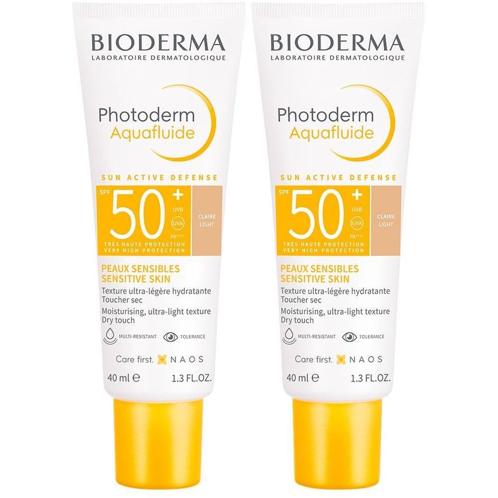 Zwei Tuben BIODERMA Photoderm Aquafluide LSF 50+ hell getönt. Weiße Tuben mit gelbem Verschluss. Produktname und SPF-Wert deutlich sichtbar.