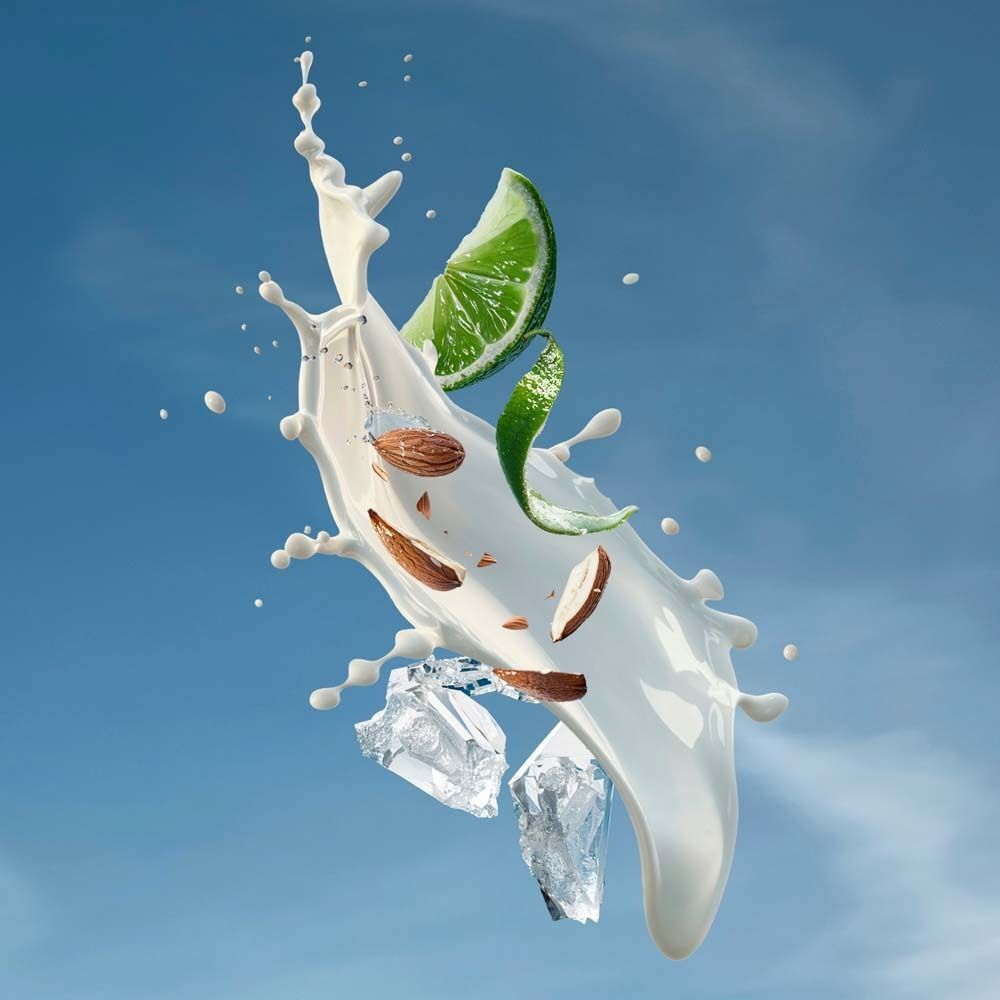 Milchspritzer mit Limettenscheibe, Mandelsplittern und Eiswürfeln vor blauem Himmel.