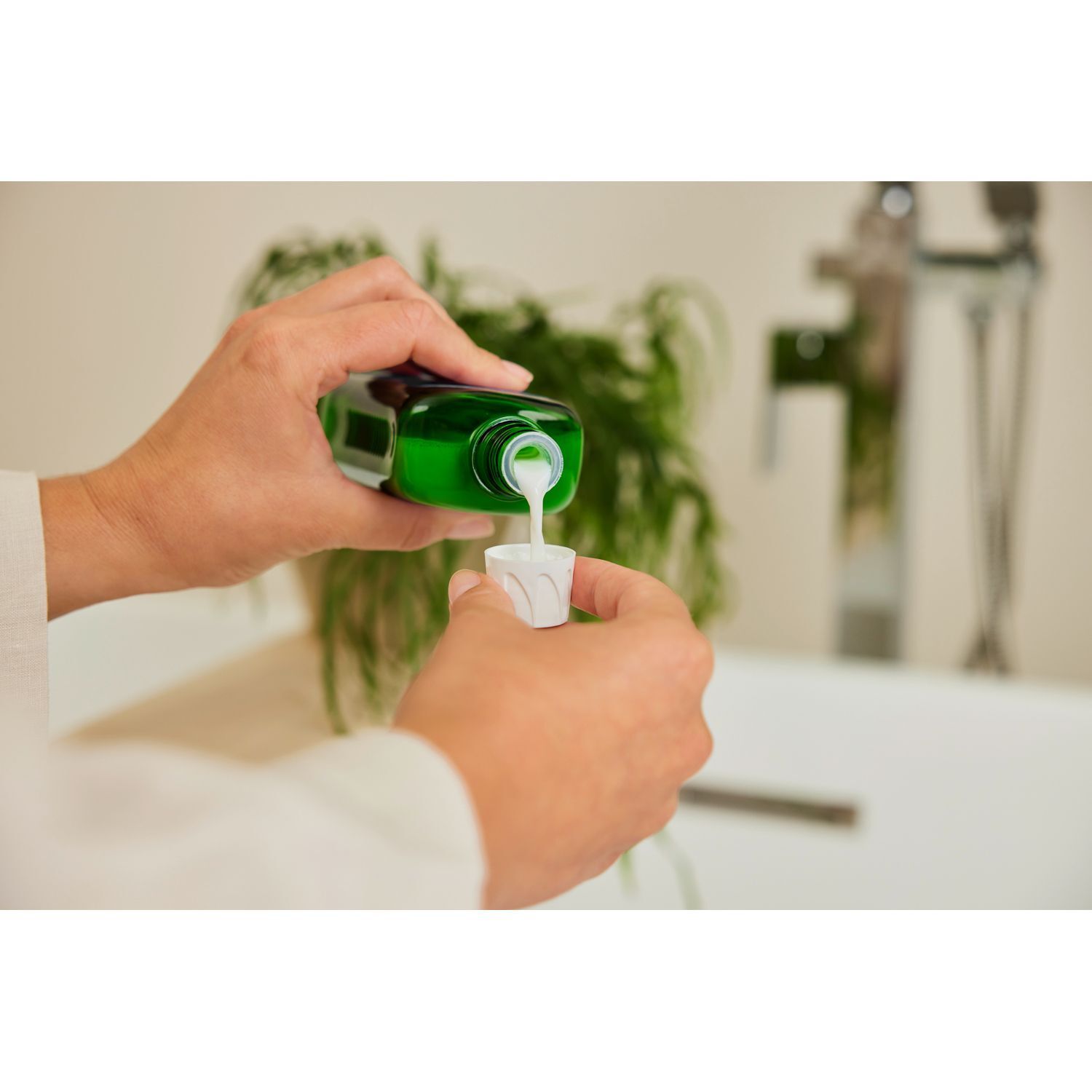 Hände gießen grüne Flüssigkeit aus einer Flasche in einen weißen Messbecher.