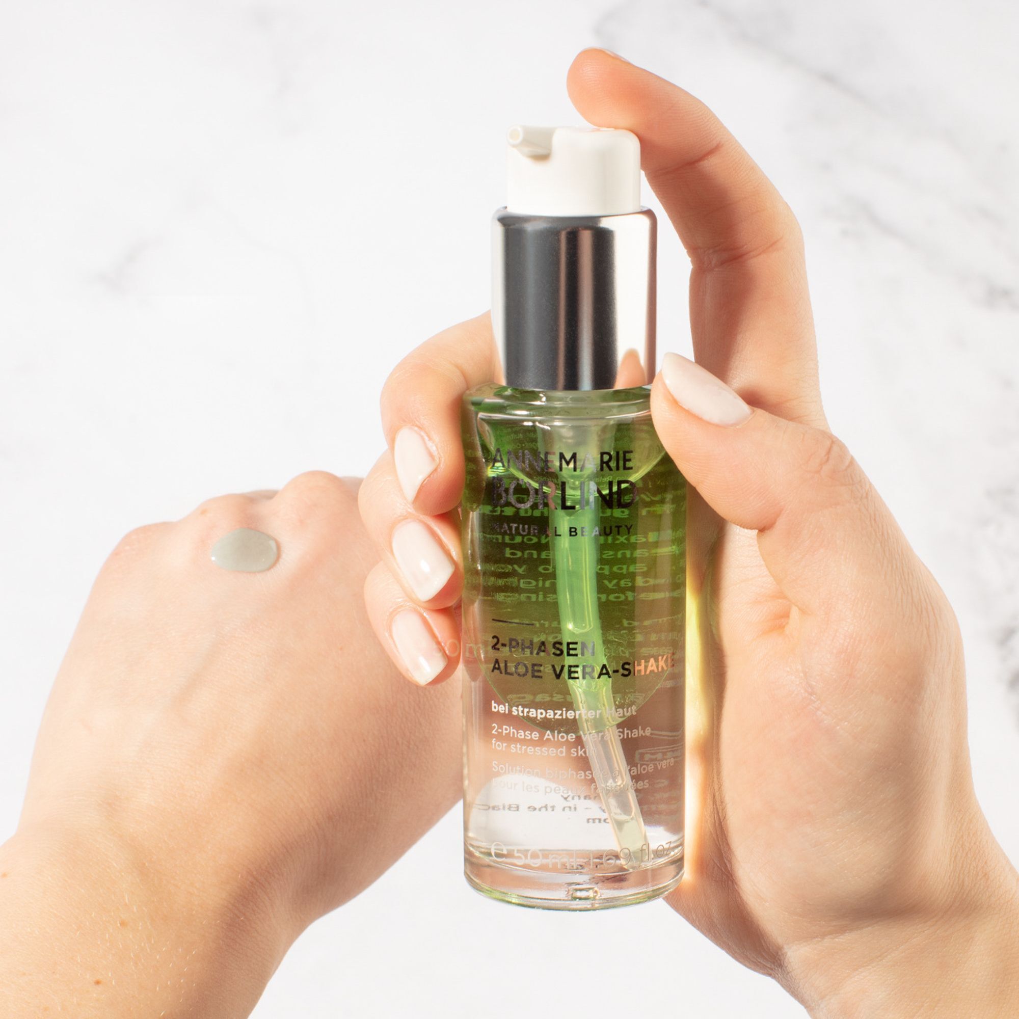 Hand hält eine Pumpflasche ANNEMARIE BÖRLIND 2-PHASEN ALOE VERA-SHAKE, mit einem Tropfen auf der anderen Hand.