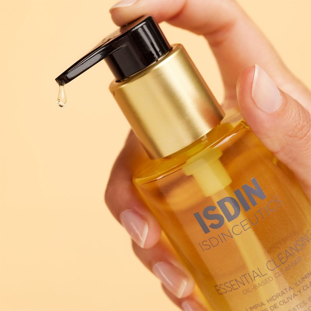 Hand hält eine Flasche ISDINCEUTICS Essential Cleansing Öl. Öl tropft aus dem Pumpkopf. Gelber Hintergrund.