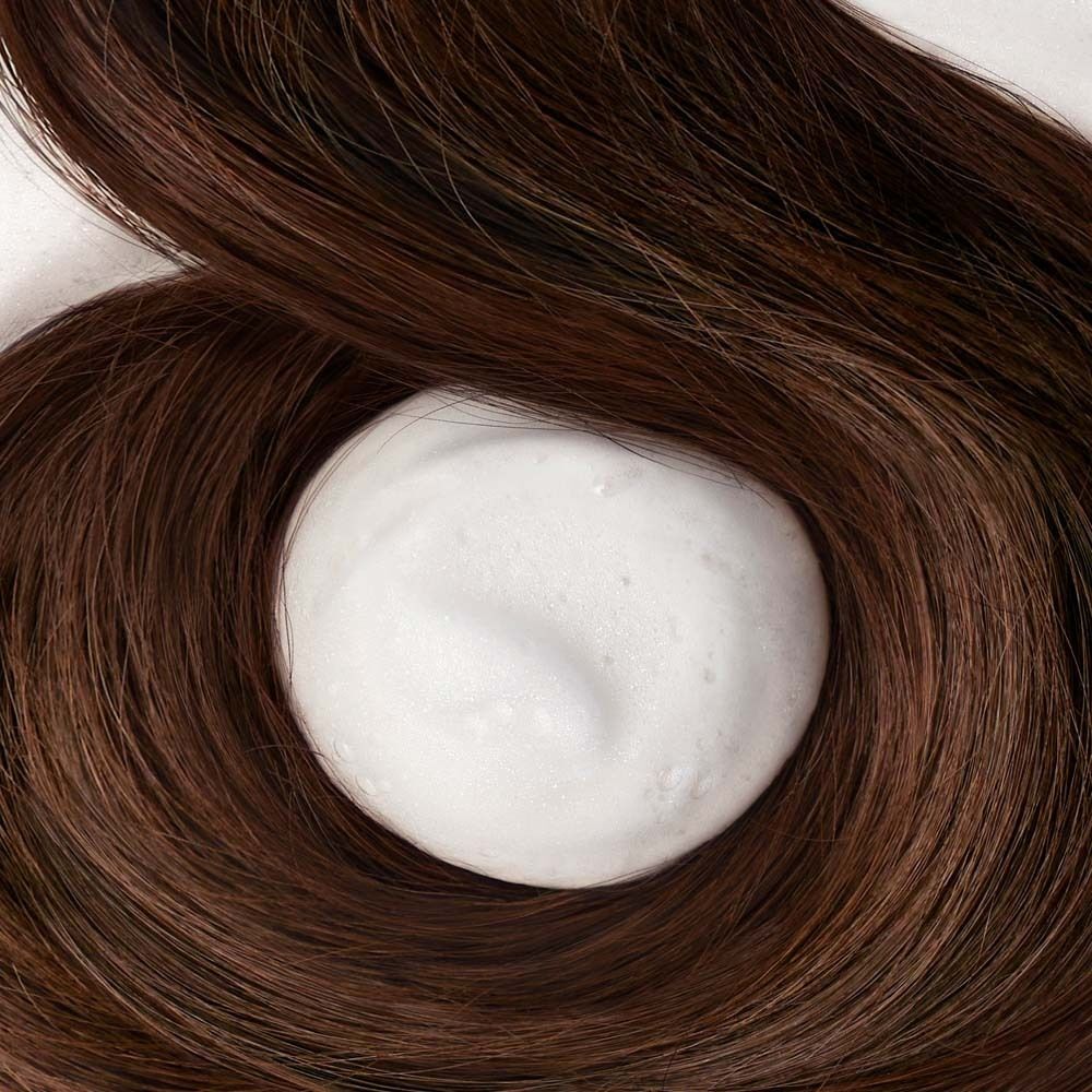 Haarsträhnen mit Schaum. Braunes Haar umgibt einen weißen Schaumkreis. Der Schaum liegt auf dem Haar.