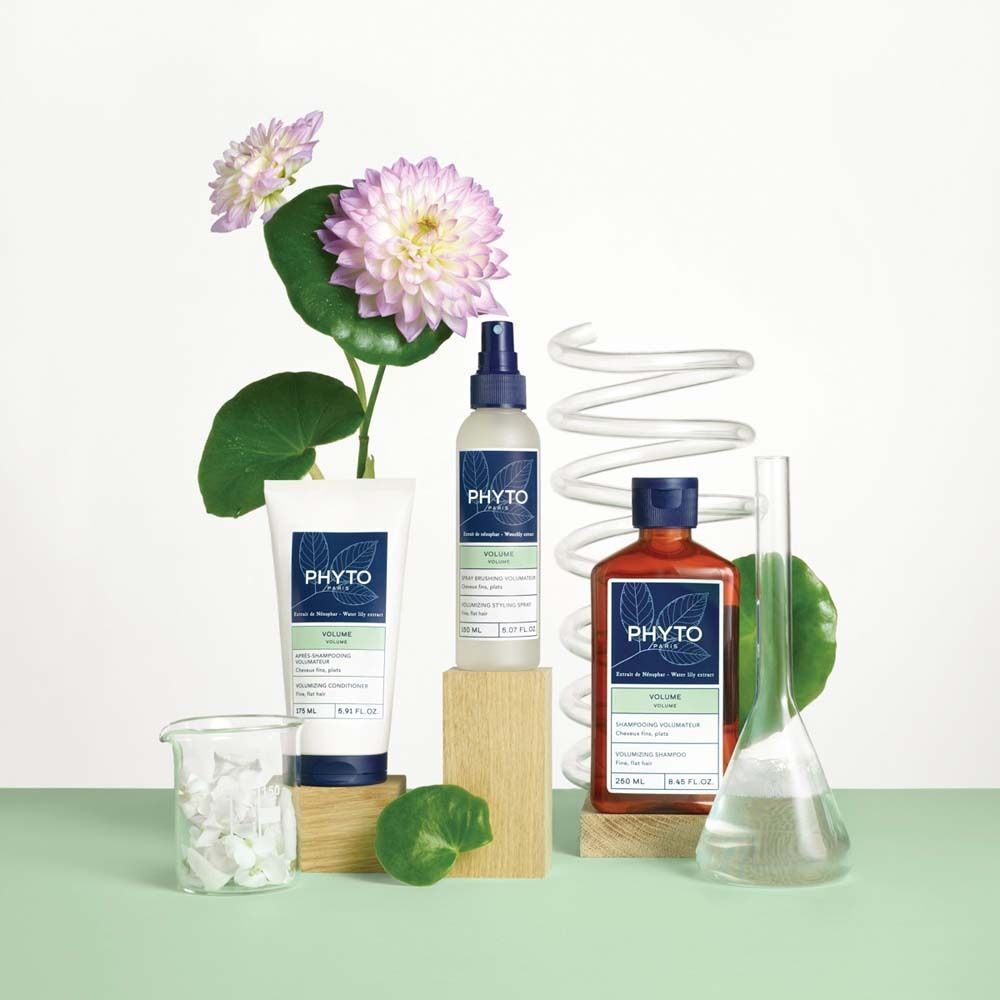 Verschiedene PHYTO PARIS Produkte. Flaschen, Tube, Sprühflasche, Blumen, Becherglas, Reagenzglas. Auf Holzblöcken platziert.