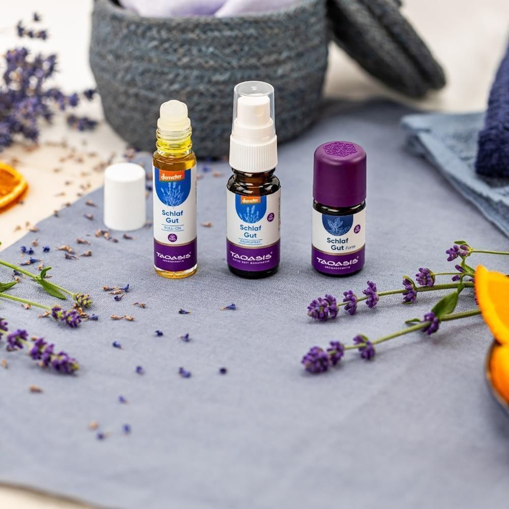 Drei Flaschen mit Etiketten: Schlaf Gut. Eine Roll-on-Flasche, eine Sprühflasche und eine Flasche mit lila Deckel. Lavendel und Dekoration.