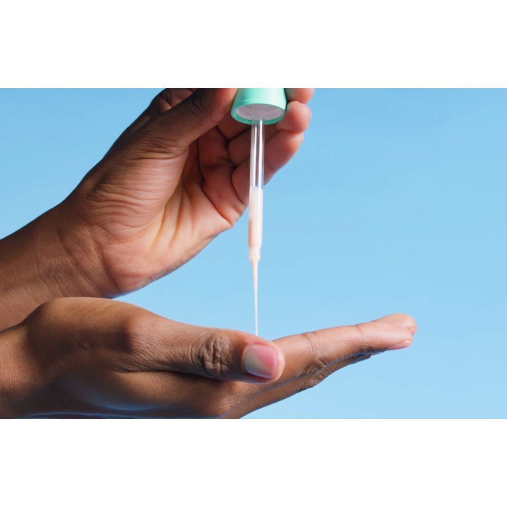 Hand hält eine Pipette mit Serum. Das Serum tropft auf die Handfläche. Helle Flüssigkeit.